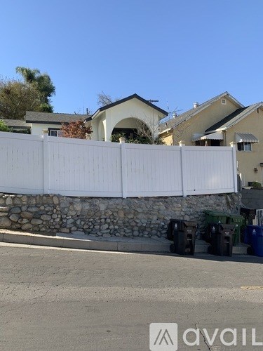 A white fence with a stone base separates a driveway from a house.