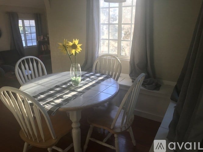 A dining table with chairs and a vase of flowers in the middle.
