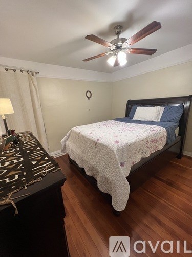 A bedroom with a bed, a ceiling fan, and a wooden floor.