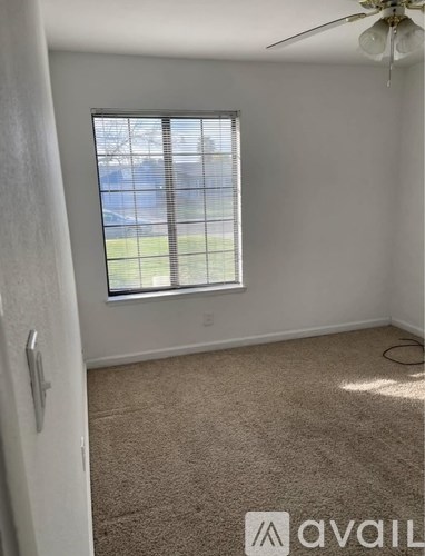 A room with a carpeted floor, a window with blinds, and a ceiling fan.