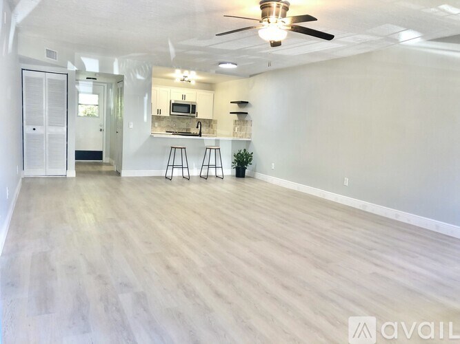 A spacious room with a ceiling fan and lighting, featuring a kitchenette with a microwave, a sink, and a countertop.