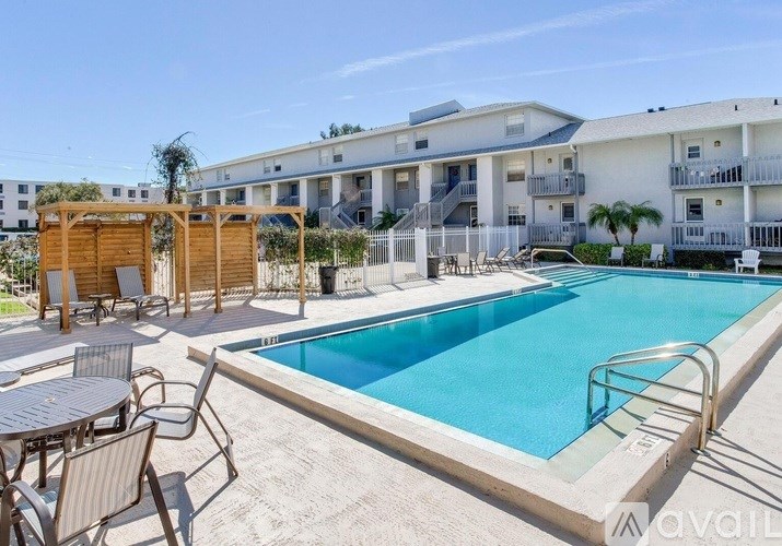 A pool area with chairs and a table is in front of apartment buildings.