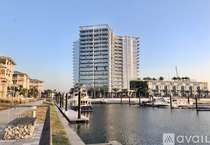 A tall building with many windows is situated next to a body of water with boats docked.