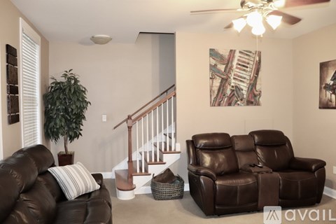 A living room with a brown leather couch and a staircase.