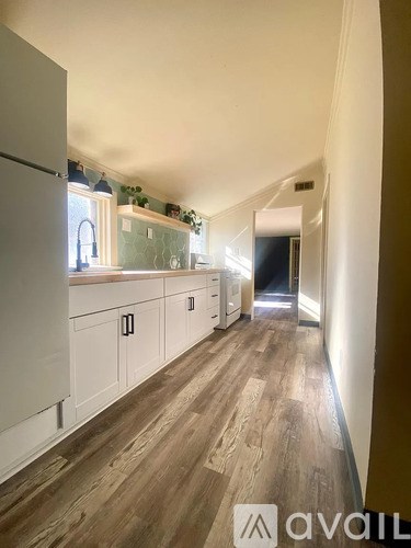 A long hallway with white cabinets and wood flooring.