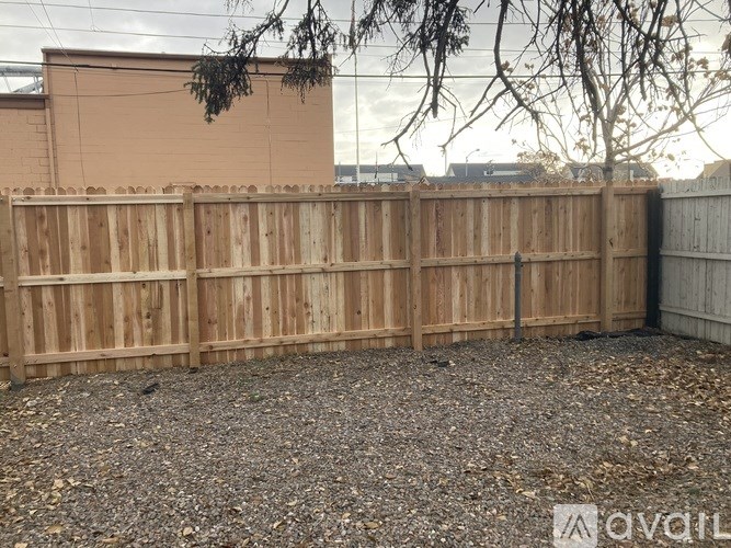 A wooden fence in front of a tan building with a tree branch hanging over it.