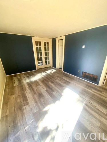 A room with wooden flooring and a doorway leading to another room.