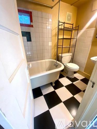 A black and white checkered bathroom floor with a bathtub, toilet, and sink.