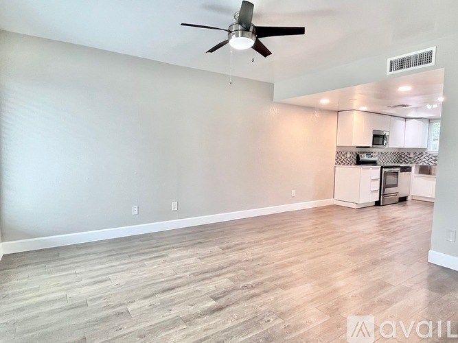 A spacious room with a ceiling fan and light fixture, and a kitchenette in the background.