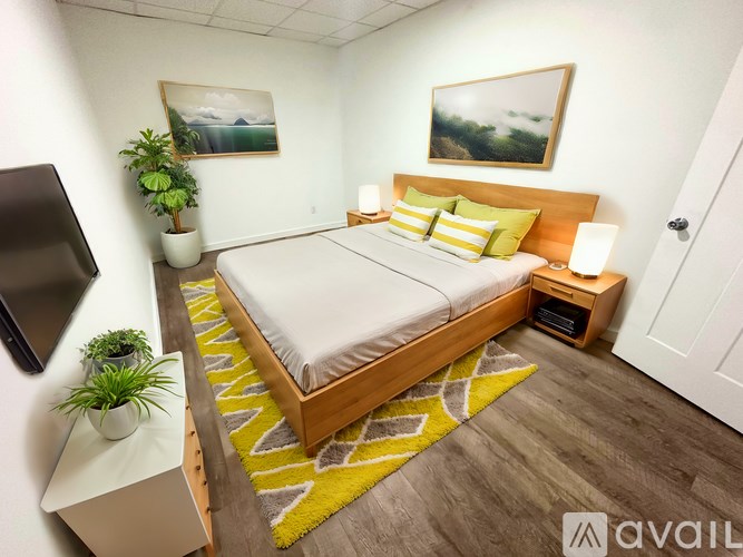 A bedroom with a bed, nightstand, and two potted plants.