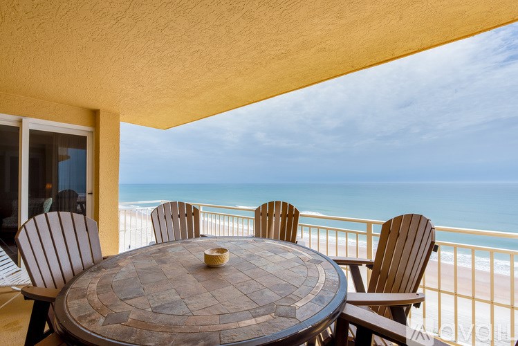 A table with chairs is set up on a balcony overlooking the beach.