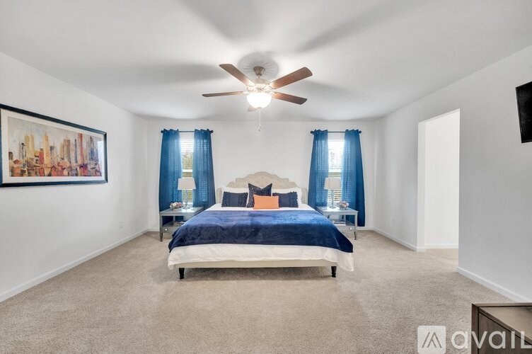 A bedroom with a bed, a ceiling fan, and a painting on the wall.