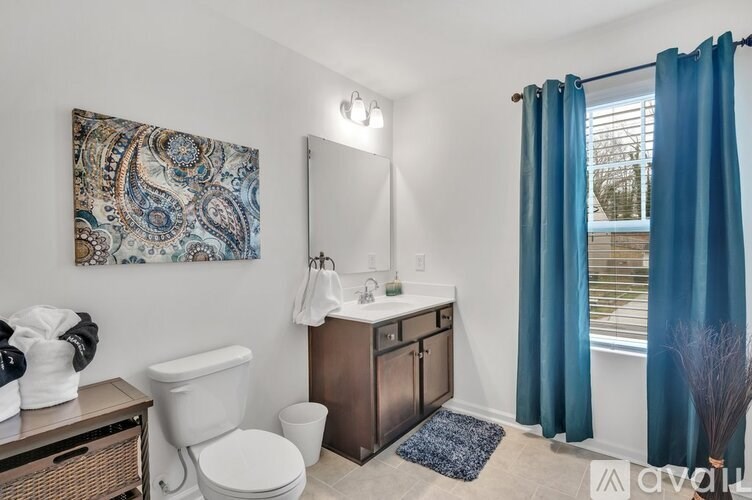 A bathroom with a white toilet, a sink with a brown cabinet, a blue rug, and a painting on the wall.