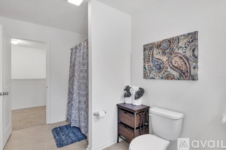 A bathroom with a white toilet, a white bathtub, a blue rug, and a paisley patterned painting on the wall.