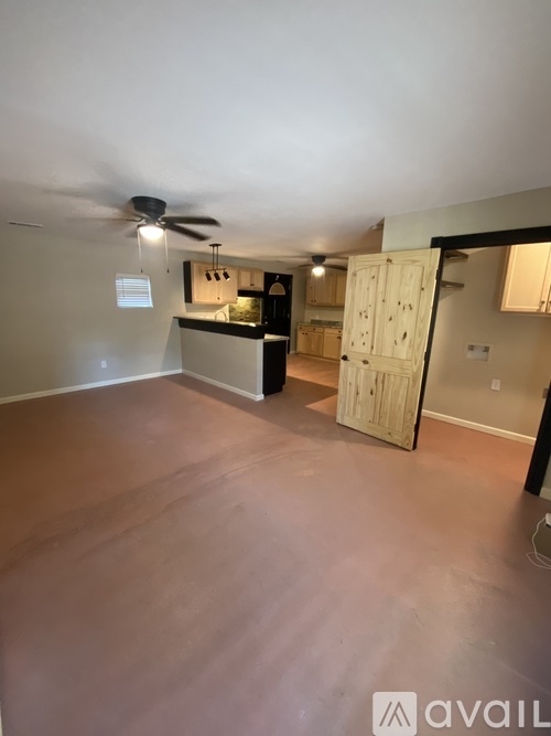 A room with a ceiling fan and a kitchenette in the background.