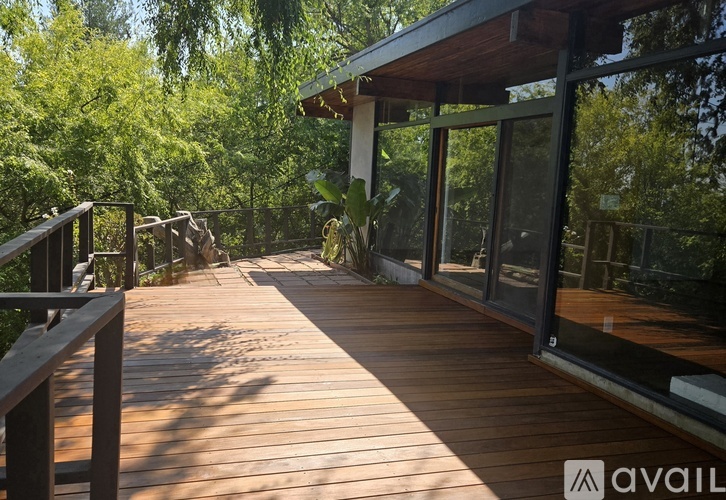 A wooden deck with a metal railing and glass doors leading to a lush green forest.
