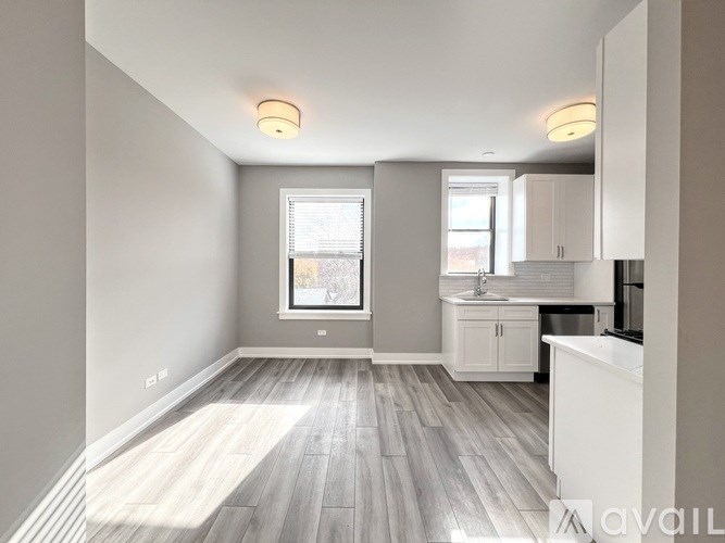 A spacious kitchen and living room with wooden flooring and white cabinetry.