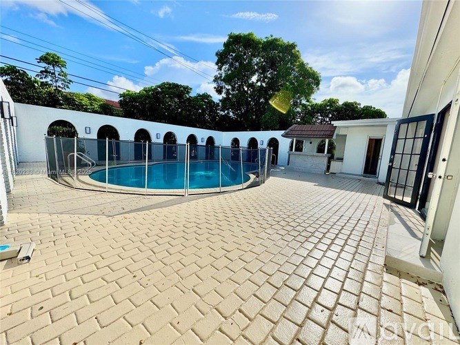 A pool surrounded by a brick patio and a white building.
