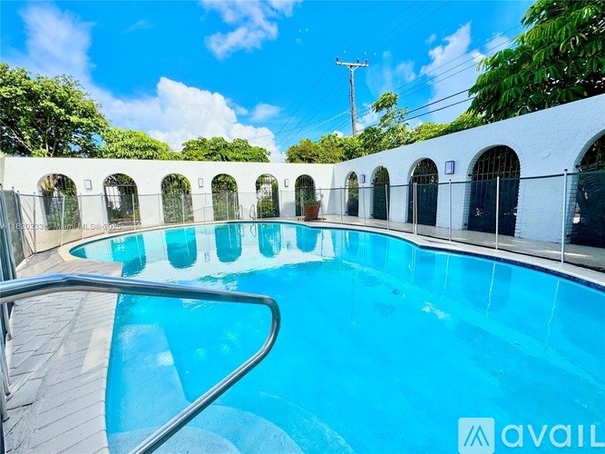 A pool surrounded by a white wall with arched windows.