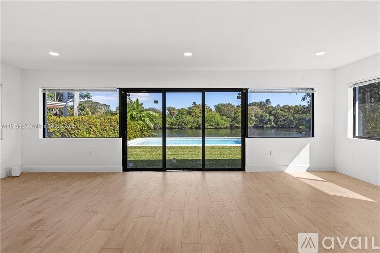A spacious room with wooden flooring and a view of a pool through a glass door.