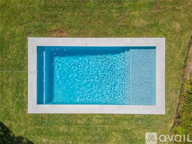 A rectangular pool with a white border is surrounded by a grassy area.