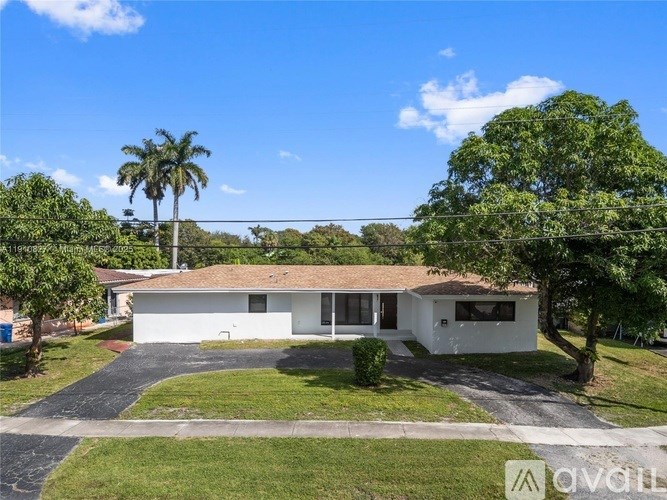 A white house with a brown roof is surrounded by greenery and trees.
