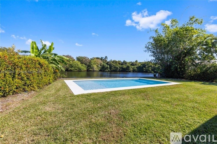 A pool surrounded by green grass and trees under a blue sky.