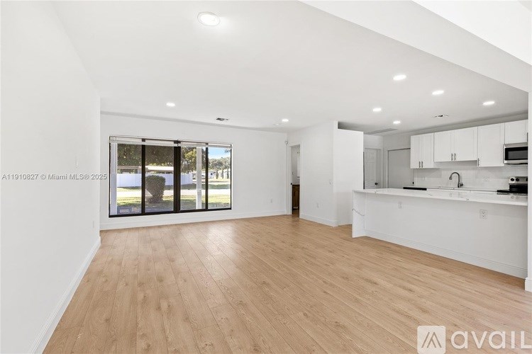 A spacious, well-lit kitchen and living area with wooden flooring and white walls.