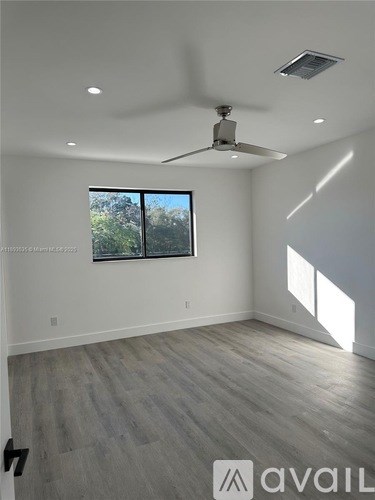 A room with a ceiling fan and a window overlooking trees.