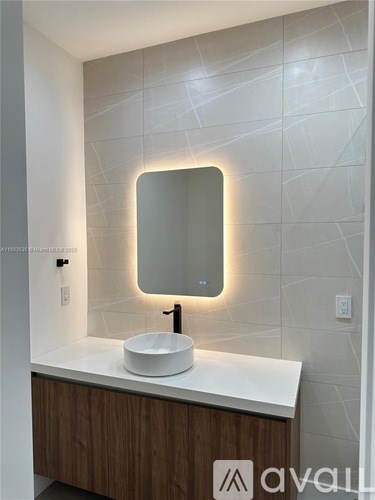 A modern bathroom with a white sink and a mirror with a light around it.