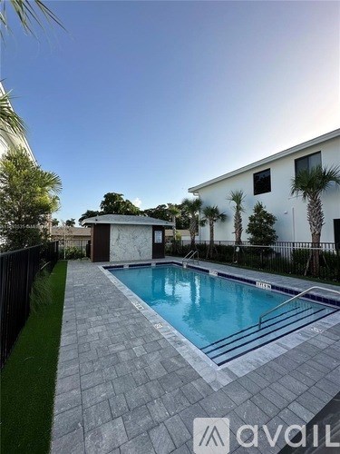 A pool surrounded by a black fence and a white house with palm trees.