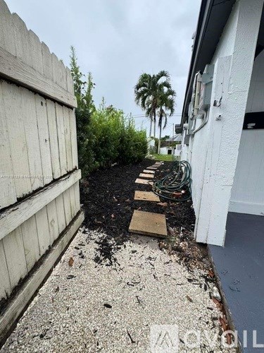 A narrow path with wooden planks leading to a white building with a door.