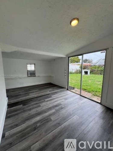 A room with wooden flooring and a sliding glass door leading to a green outdoor area.