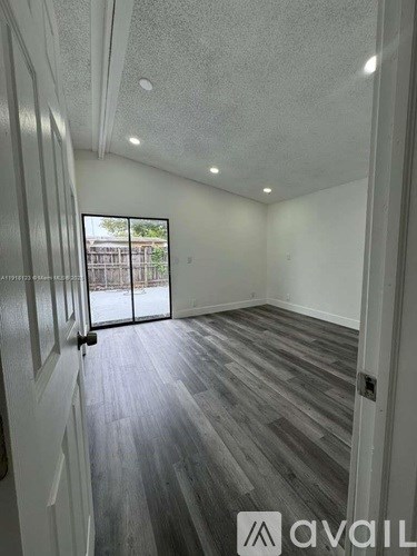 A room with wooden flooring and white walls, with a sliding glass door leading outside.