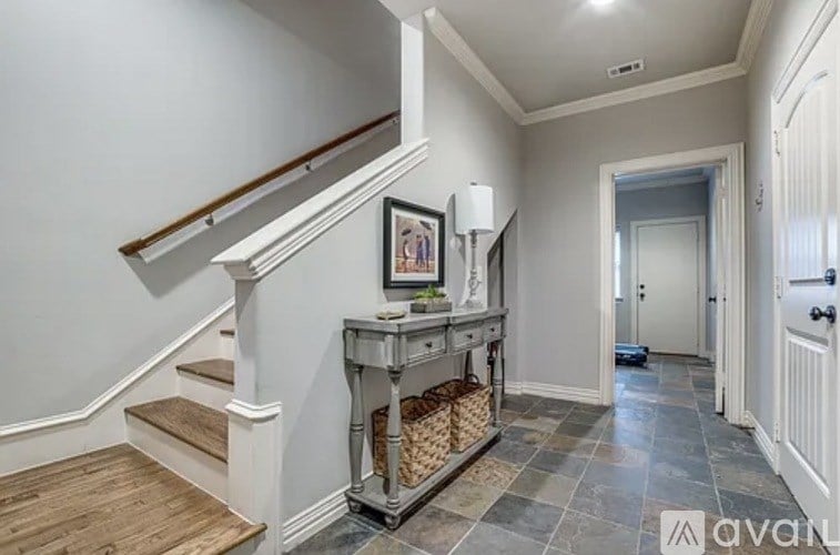 A hallway with a staircase and a console table with a basket underneath it.