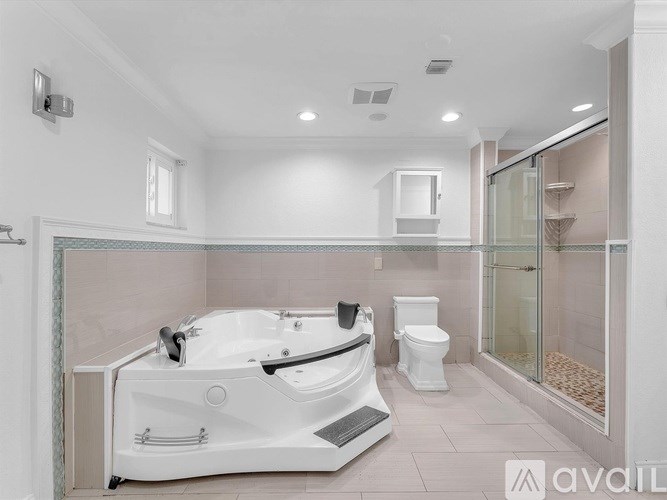 A white bathtub with a black faucet is in a bathroom with a toilet and a walk-in shower.