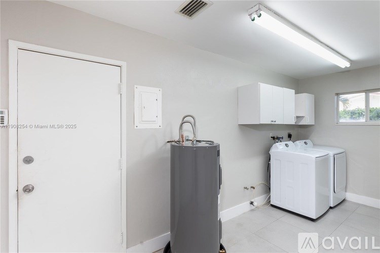 A room with a white door, a grey fridge, and a white cabinet with a window.