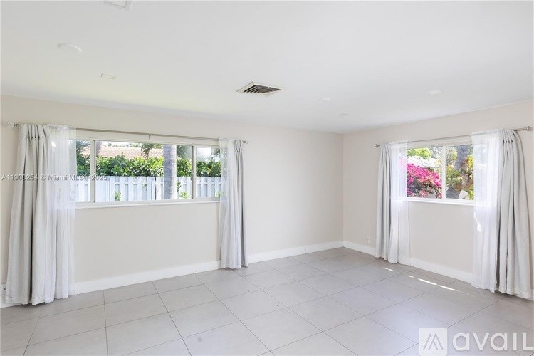 A spacious room with white walls and a large window with white curtains.