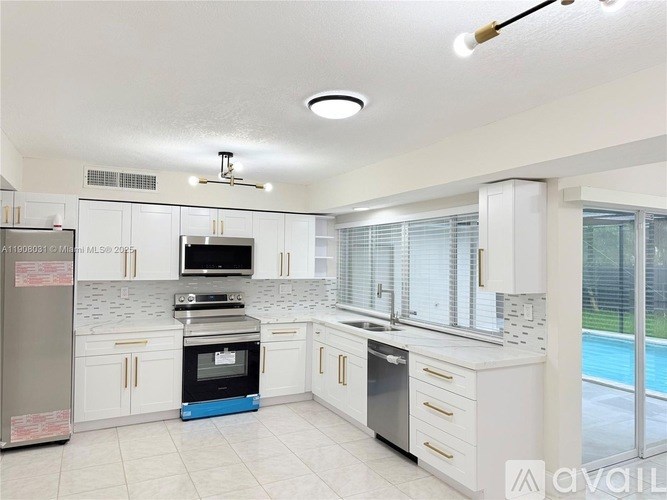 A kitchen with white cabinets and appliances, a blue oven, and a pool outside the window.