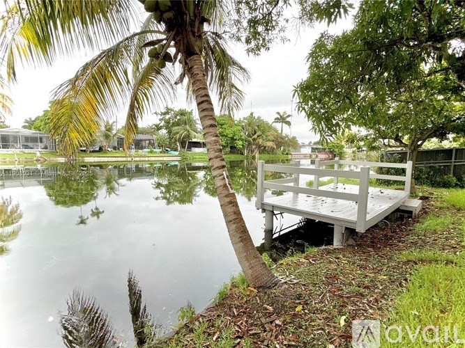 A wooden dock extends into a calm body of water surrounded by lush greenery.