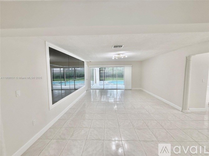 A spacious room with white walls and a tiled floor leading to a glass door.