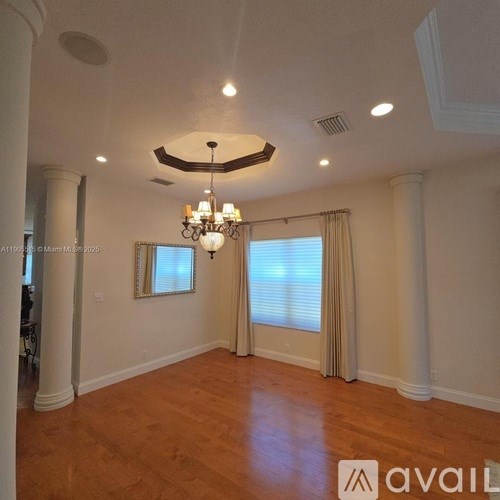 A large empty room with wooden floors and a chandelier hanging from the ceiling.