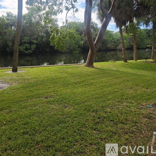 A grassy area with trees and a body of water in the distance.