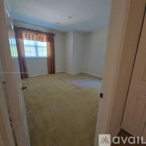 A room with a carpeted floor and a window with curtains.