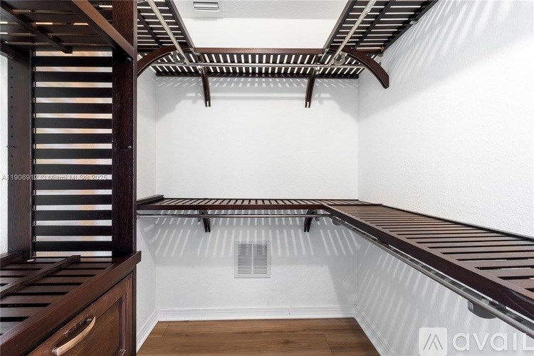 A room with a white wall and a wooden floor has a shelf and a staircase.