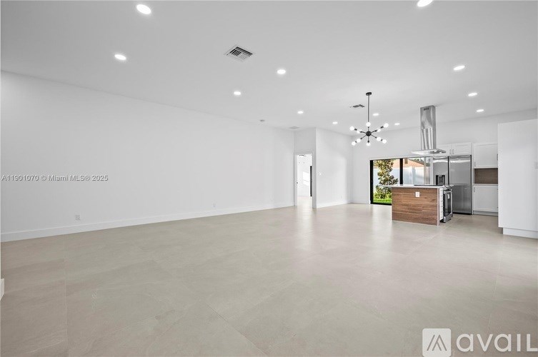 A spacious, empty room with a kitchen area in the background.