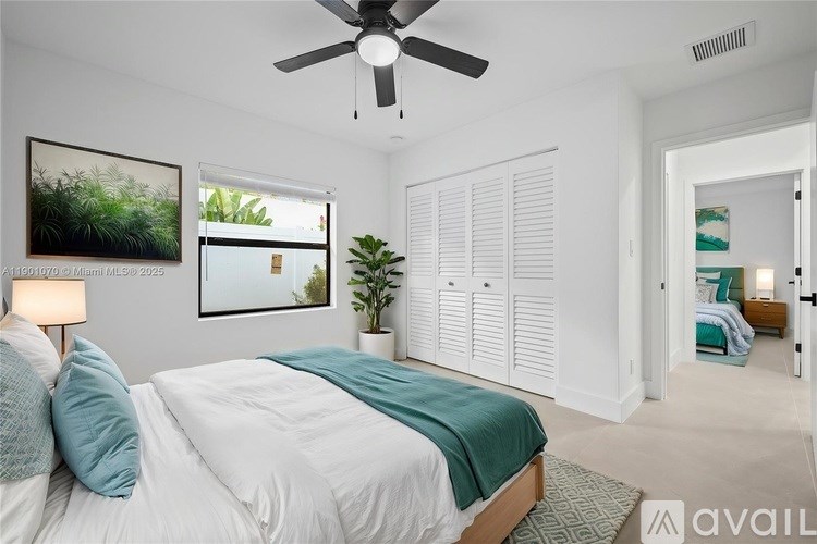 A bedroom with a bed, a ceiling fan, and a painting on the wall.