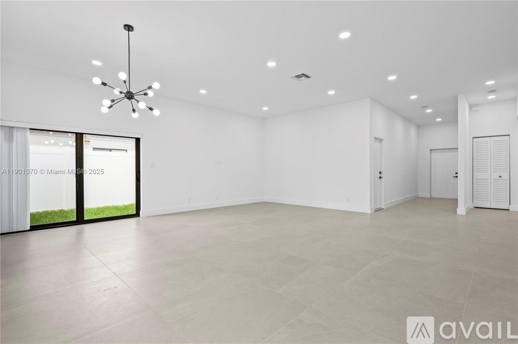 A spacious room with a chandelier and a view of greenery outside the window.