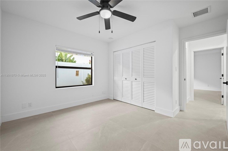 A room with a ceiling fan and a window showing greenery outside.