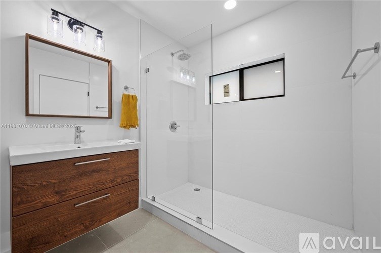 A bathroom with a white sink, a mirror, a shower, and a yellow towel.